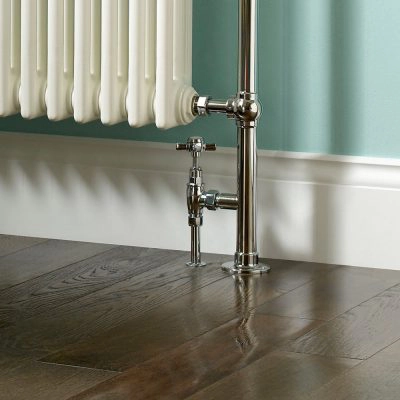 Close-up of chrome radiator valve and pipework on dark wood flooring